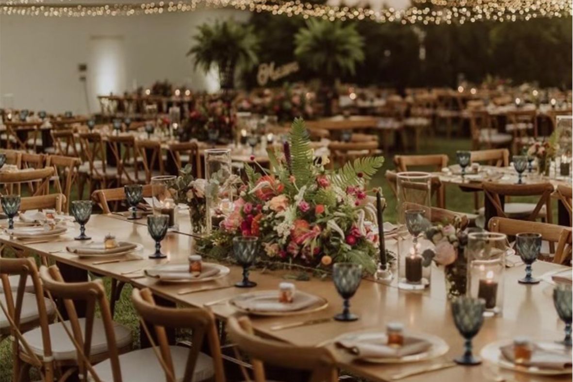 Garden wedding reception with long wooden tables, grey glassware and a coral flower garland